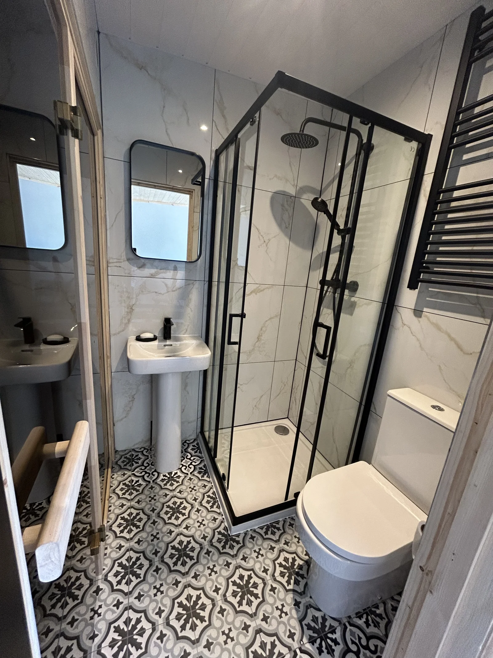 Compact bathroom with marble-look tiles, black fixtures and corner shower